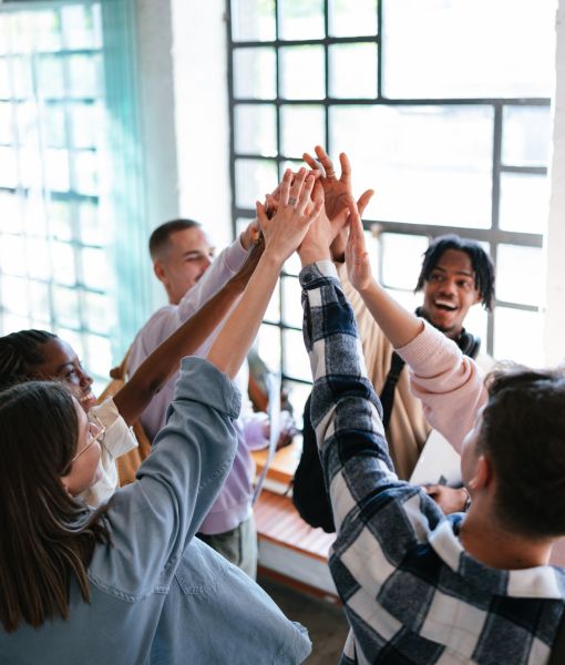  Junges Team gibt sich lachend ein High five nach dem erfolgreichen Projektabschluss.